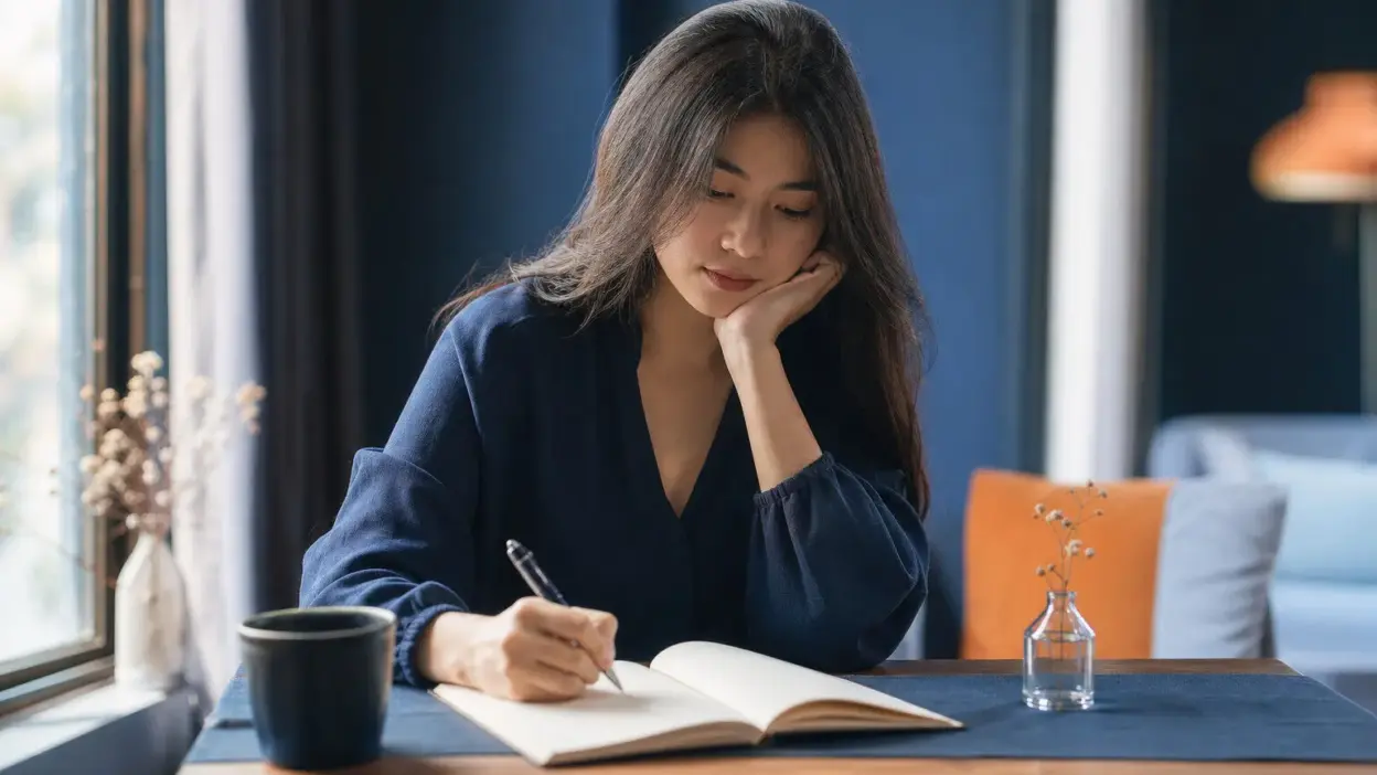 Mahasiswa duduk dekat jendela menulis jurnal, merenungkan insight psikologi praktis dari semangat psychosociopreneur