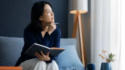 Seorang orang tua duduk dekat jendela menulis jurnal, merefleksikan rasa bersalah dan pengasuhan dari perspektif insight psikologi praktis