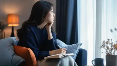 Seorang dewasa duduk dekat jendela menulis jurnal, merefleksikan psikologi modern dan akses ilmu psikologi