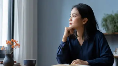 Seorang relawan pendamping duduk dekat jendela menulis jurnal sebagai refleksi diri untuk mengolah beban empati
